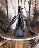 Black leather bag with handles on a wooden stand against a rustic background