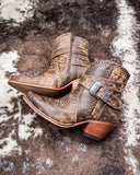 Pair of brown leather boots with buckles on a textured surface