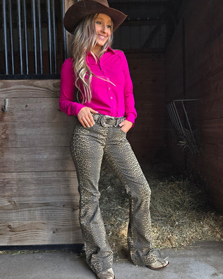 Woman in pink shirt and patterned pants standing in a barn.