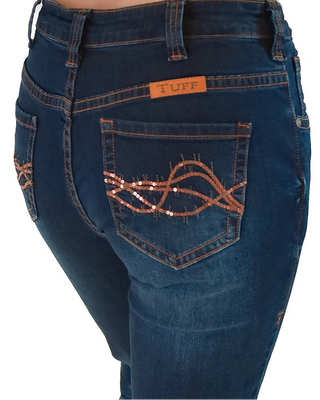 Close-up back view of a person wearing dark blue denim jeans with a tan leather patch reading TUFF on the back pocket and copper sequined decorative stitching on the pocket.