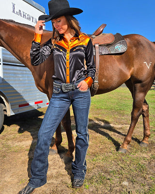 Woman in cowboy attire standing next to a horse with a Lakota trailer in the background
