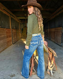 Woman in a cowboy hat and blue jeans standing in a stable with a saddle.