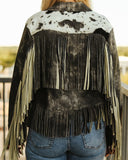 Person wearing a black and white cowhide leather jacket with fringes.