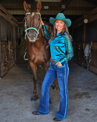 Woman in turquoise outfit standing next to a horse in a stable