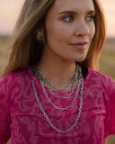 Woman wearing a pink top with a pattern and layered necklaces outdoors.
