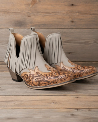 Pair of beige cowboy boots with brown leather detailing on a white background