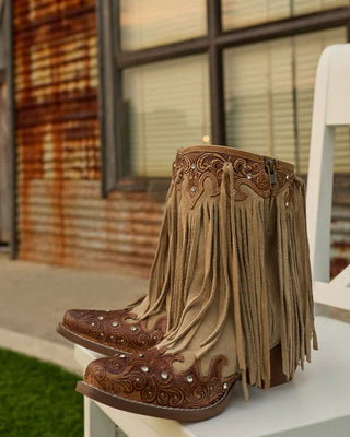 Pair of brown fringe boots on a white chair with a rustic building background