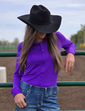 A cowgirl leaning on a fence, wearing the High Stakes Hue Pullover Button Up. 