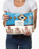 A person holding the bagged Cactus Stripe Travel Blanket in a white backdrop.