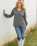 The Hadley Top in Charcoal being styled and worn by a women next to a wall background.