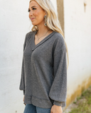 The Hadley Top in Charcoal being styled and worn by a women next to a wall background.