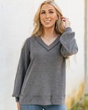 The Hadley Top in Charcoal being styled and worn by a women next to a wall background.