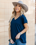 The Thatcher Top in navy being styled and modeled on a women in front of brick background.