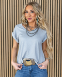 The Sloan Top in Pearl Grey being styled and worn by a women in front of wood background.