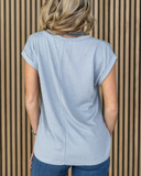 The Sloan Top in Pearl Grey being styled and worn by a women in front of wood background.