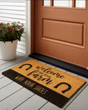 Welcome to Our Farm Coir Doormat on a wooden floor outside a door.