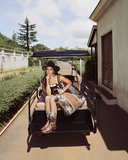 Woman sitting in a golf cart on a sunny day with trees and a building in the background.