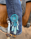 Close-up of a blue dreamcatcher design on a pair of jeans with a horse in the background.