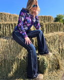 Woman sitting on a stack of hay wearing a colorful jacket and jeans.