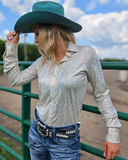 Woman wearing a sparkly silver shirt, blue jeans, and a teal cowboy hat in an outdoor setting.
