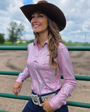 Woman in a pink long-sleeve shirt and cowboy hat standing in an outdoor setting.