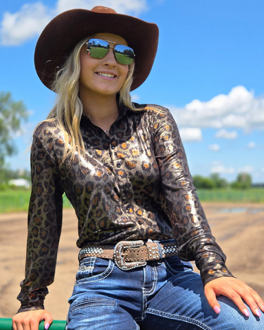 Woman in leopard print shirt and cowboy hat sitting outdoors on a sunny day.