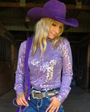 Woman wearing a purple cowboy hat and shirt, holding a purple rope in a barn setting.