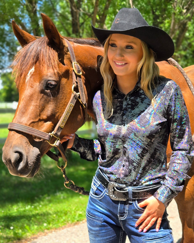 Woman in cowboy hat and chrome shirt standing next to a horse outdoors