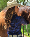 Woman in a blue shirt and cowboy hat petting a brown horse outdoors.