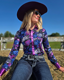 Woman in a colorful shirt and cowboy hat sitting on a hay bale with a blue sky background