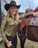 Woman in a cowboy hat and patterned shirt standing next to a horse with a saddle.