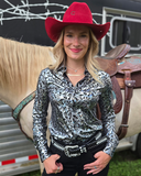 Woman wearing a red cowboy hat and patterned shirt standing next to a horse with a trailer in the background.
