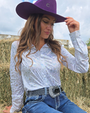 Woman wearing a purple cowboy hat and white long-sleeve shirt in an outdoor setting.