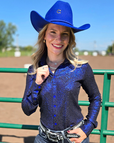 Woman wearing a blue glitter shirt and cowboy hat in an outdoor setting