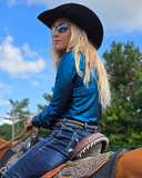 Person wearing a black cowboy hat and teal shirt sitting on a horse with a scenic background