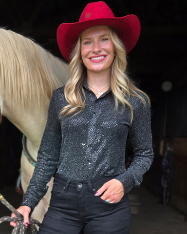 Woman wearing a red cowboy hat and sparkly black shirt standing next to a horse.