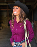 Woman wearing a burgundy shirt and black cowboy hat with a rope halter, standing in a barn.