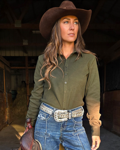 Woman wearing a green shirt, blue jeans, and a brown cowboy hat in an indoor setting.
