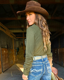 Woman wearing a cowboy hat and green shirt in a stable setting