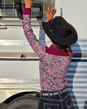 Person wearing a patterned shirt and black hat standing next to a silver trailer.