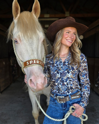 Woman in a cowboy hat standing next to a horse named 'Spirit' in a stable.