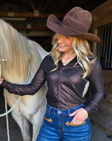 Woman in cowboy hat and dark long-sleeve shirt standing next to a horse in a barn.