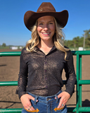 Woman wearing a brown cowboy hat and dark long-sleeve shirt standing in front of a green metal gate with a clear blue sky.