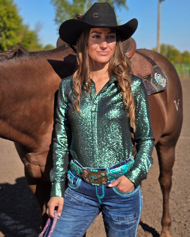 Woman in a green shimmer shirt and black cowboy hat standing next to a horse.