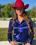 Person wearing a red cowboy hat and blue satin shirt outdoors