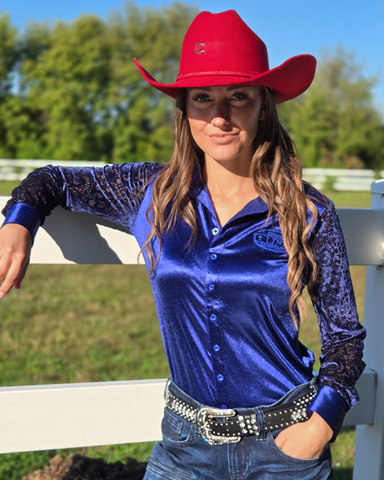 Woman wearing a blue shirt and red cowboy hat with a white fence and trees in the background