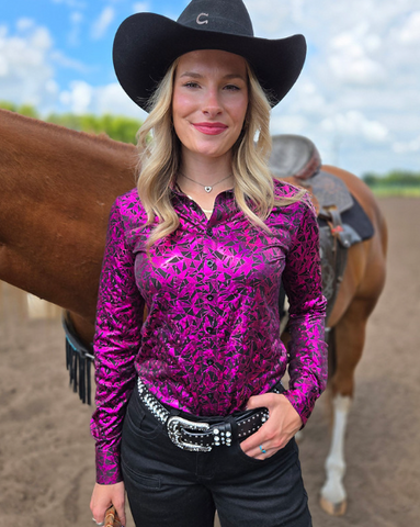 Woman in a pink patterned shirt and black cowboy hat standing next to a horse.