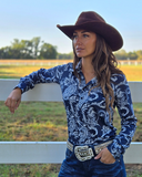 Woman wearing a navy paisley print shirt standing in front of a white fence.