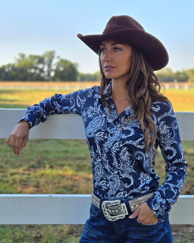 Woman wearing a navy paisley print shirt standing in front of a white fence.