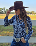 Woman wearing a navy paisley print shirt standing in front of a white fence.